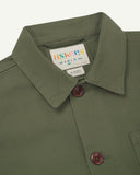Close up view of an Uskees green overshirt collar with a visible brand label on a white background
