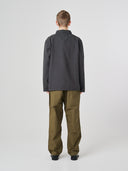 Full-length back view of man wearing an Uskees charcoal-grey cotton overshirt paired with khaki-green pants, showing reinforced elbows.