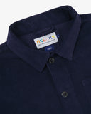 Close-up top-half view of #3001 deep indigo organic cotton corduroy overshirt. With focus on collar, hanging loop, Uskees brand label and corozo buttons.
