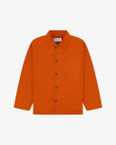 Front flat shot of golden-orange, buttoned organic cotton overshirt. Clear view of chest and hip pockets, corozo buttons and Uskees branding label.