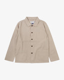 Front flat shot of oatmeal (beige), buttoned drill overshirt. Clear view of corozo buttons, 3 pockets and Uskees branding label.