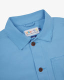 Close-up view of 3001 powder blue, buttoned organic cotton overshirt from Uskees showing corozo buttons, brand label, collar and hanging hoop.