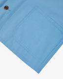 Closer view bottom-right section of powder blue, buttoned organic cotton overshirt from Uskees. Focus on hem, hip pocket and corozo buttons.