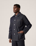 Side view of male model wearing Uskees raw orta denim workwear pants in dark indigo with matching denim overshirt. 