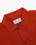 Close-up view of 3001 rust-red, buttoned organic cotton overshirt from Uskees showing corozo buttons, brand label, collar and hanging hoop.