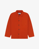 Front flat shot of rust-red, buttoned organic cotton overshirt. Clear view of chest and hip pockets, corozo buttons and Uskees branding label.