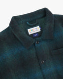 Close-up view of 3001 peacock blue check, buttoned Pennine wool overshirt from Uskees showing corozo buttons, brand/size label, collar and hanging hoop.