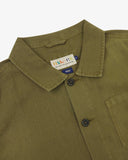 Close up view of an Uskees green linen overshirt for men showing the brand label the collar and Corozo buttons.