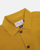 Close-up view of 3001 yellow, buttoned organic cotton overshirt from Uskees showing corozo buttons, brand label, collar and hanging hoop.