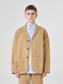 Top-half view of man wearing khaki buttoned organic cotton-twill blazer. Jacket unbuttoned to reveal pale blue Uskees shirt.