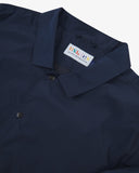 Close up flat shot of Uskees navy blue coach jacket for men with focus on collar, contrast inner yoke, Uskees brand label and popper buttons.