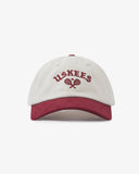 Front view of cream and maroon Uskees 6-panel cap with 'USKEES' and tennis racquet motif embroidered in maroon.