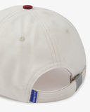 Close-up back view of cream and maroon Uskees cap with focus on the cord material, vents, adjustable strap with metal fastener and 'USKEES' logo tab.