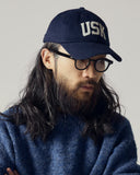 Model wearing cream Uskees 6-panel cap with 'USK' embroidered motif in cream.