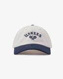 Front view of cream and navy blue Uskees 6-panel cap with 'USKEES' and tennis racquet motif embroidered in navy blue.