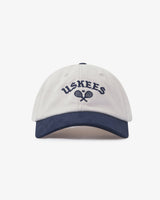 Front view of cream and navy blue Uskees 6-panel cap with 'USKEES' and tennis racquet motif embroidered in navy blue.