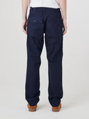 Close-up back view of model wearing Uskees twill workwear pants in deep blue showing the buttoned back pocket and waist adjuster buttons.