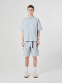 Full-length front view of a male model wearing an Uskees pale blue-grey short-sleeve button front trek shirt paired with matching Uskees technical shorts.