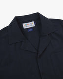Close-up shot of Uskees dark blue Cuban shirt with focus on the notched collar, brand label and hanging loop.