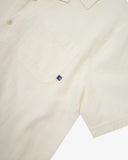Front close up shot of Uskees cream linen blend short-sleeve Cuban shirt showing the chest pocket with brand tab.