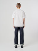 Full-length back view of model wearing an Uskees off-white Cuban shirt paired with indigo raw orta Uskees jeans.