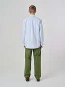 Back view of man wearing Uskees light blue and white striped men's Oxford shirt, paired with Uskees green pants.