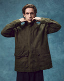 Front view of man wearing the Uskees wax storm jacket in dark 'Pennine' green. Jacket fastened, clearly showing the large flap pockets and storm collar.
