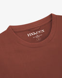 Neckline close-up of Uskees chestnut-brown organic cotton T-shirt showing hanging loop and branding stamp.