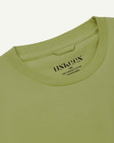 Neckline close-up of Uskees green-yellow organic cotton T-shirt showing hanging loop and branding stamp.