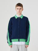 Male model showing top half wearing an Uskees navy and green track jacket with light gray shorts on a white background