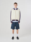 Male model wearing a cream track jacket with light blue shorts on a white background