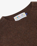 Close up view of Uskees 7021 Skye lambswool sweater in brown, with focus on crew neck and branding label.