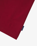View of hemline of Uskees red cotton T-shirt with focus on cotton jersey fabric and blue 'USKEES' logo tab on the seam.