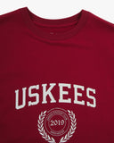 Neckline close-up of red organic cotton T-shirt, with focus on the neck tape reinforcement and Uskees Racquet Club brand graphics in white.