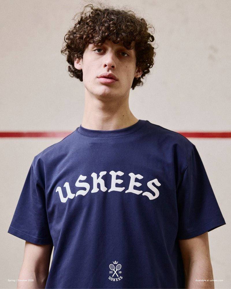 Model wearing the Uskees navy blue organic cotton T-shirt for men, showing the brand graphics on front and loose silhouette.