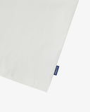 View of hemline of Uskees white cotton T-shirt with focus on cotton jersey fabric and blue 'USKEES' logo tab on the seam.