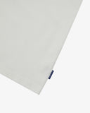View of hemline of Uskees white cotton T-shirt with focus on cotton jersey fabric and blue 'USKEES' logo tab on the seam.