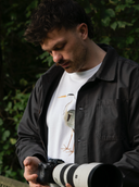 Model holding camera wearing white t-shirt with heron graphic print on chest
