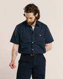 Male model wearing an Uskees navy short-sleeve shirt and pants on a beige background.