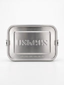 A brushed stainless steel lidded container with rounded corners, shown closed on a clean white background. The lid features the embossed brand name 'USKEES' and the text 'FOR A RICH AND FULFILLING LIFE' near the bottom.